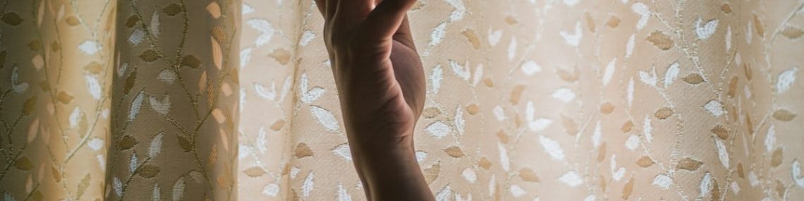 persons hand on white and brown floral curtain